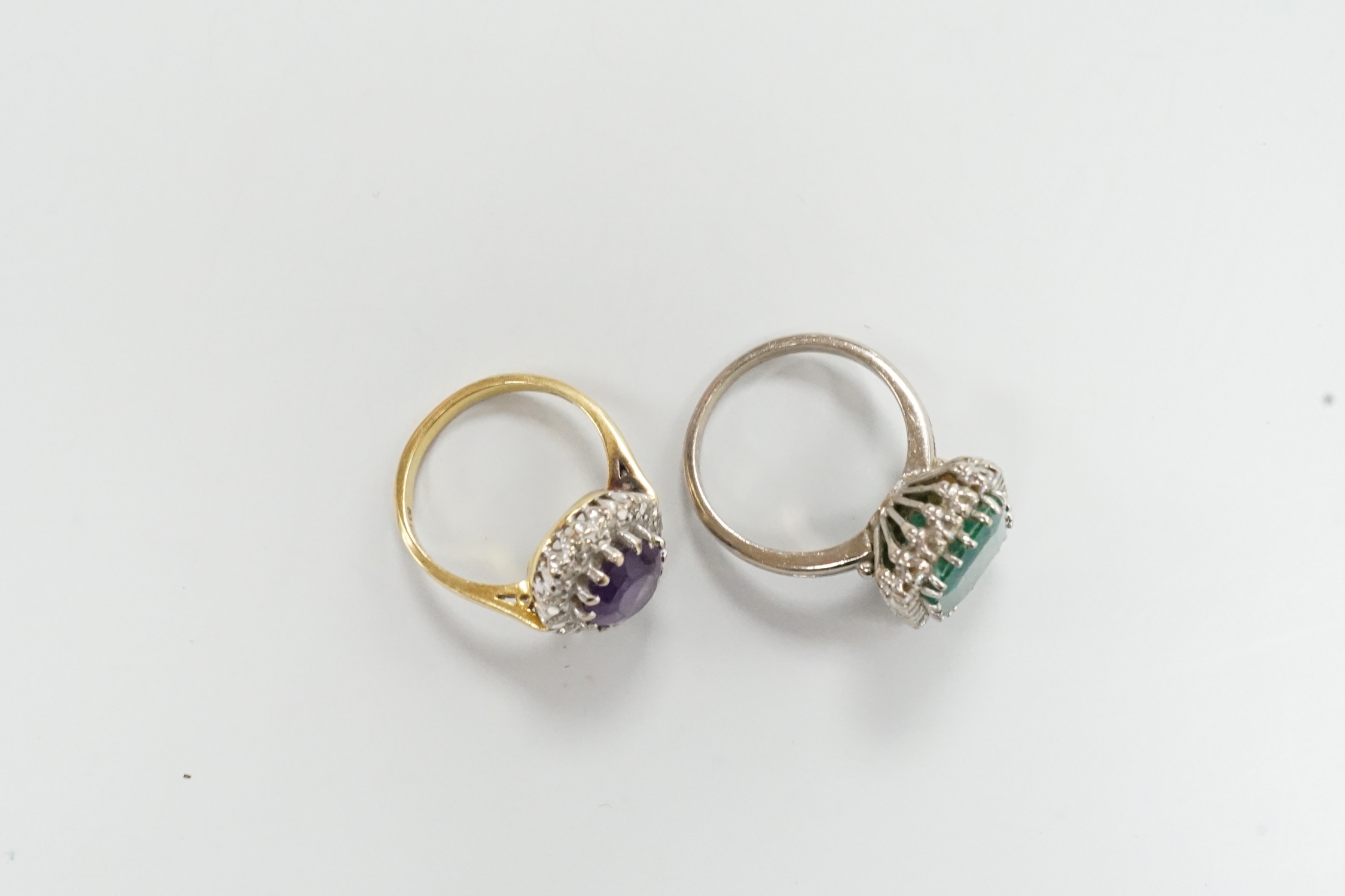 A modern 18ct gold, amethyst and diamond set oval cluster ring, size K/L and a white metal, emerald and diamond cluster set ring, gross weight 11.8 grams.